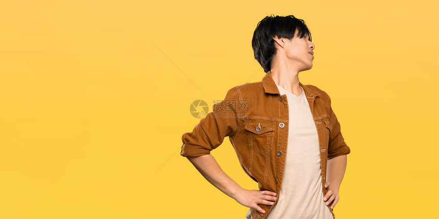 穿着棕色外套的亚裔男子因努力克服孤立的黄色背景而患背痛图片