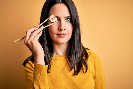 蓝眼睛的棕发年轻女人蓝眼睛吃大马鸡鱼寿司用筷子和自信的表情在聪明的面图片