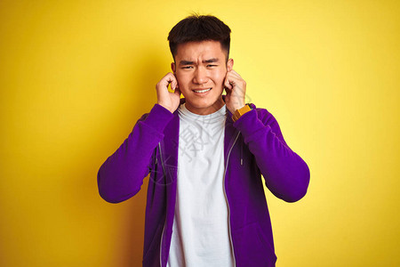 身穿紫色运动衫的年轻亚洲华裔男子站在孤立的黄色背景上图片
