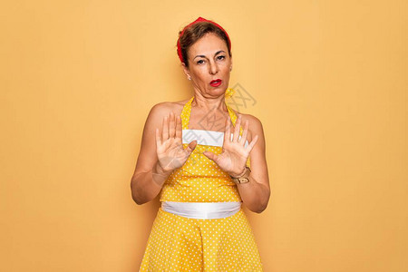 中年高级别针女人穿着50年代风格的复古连衣裙在黄色背景上移开手掌图片