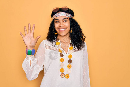 身着太阳镜和古董饰品的年轻非裔美国卷发嬉皮女郎展示并举起五指头背景图片