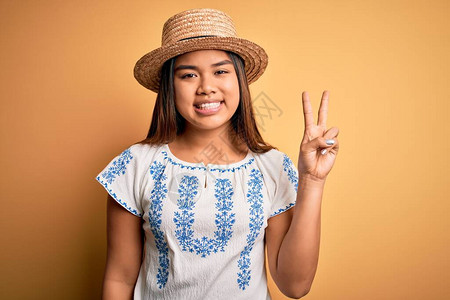 身穿轻便T恤衫和帽子的年轻美丽的亚洲女孩站在黄色背景展上图片
