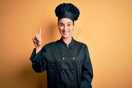 身穿厨具制服和帽子的年轻女厨师站在黄色背景展出前图片