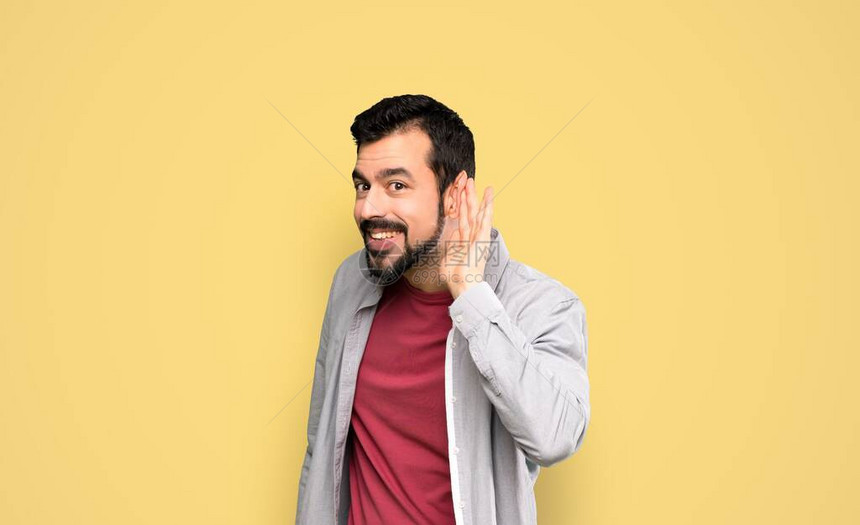 长着胡子的帅哥在独白黄色背景上用手把耳朵放在耳朵上图片