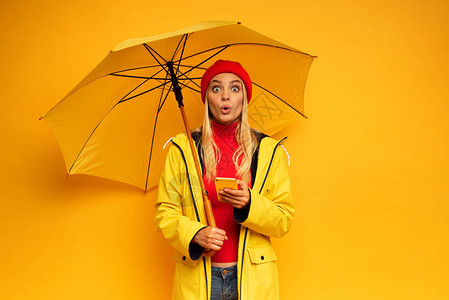 黄色背景的有智能手机和雨伞的女孩对雨季感到图片