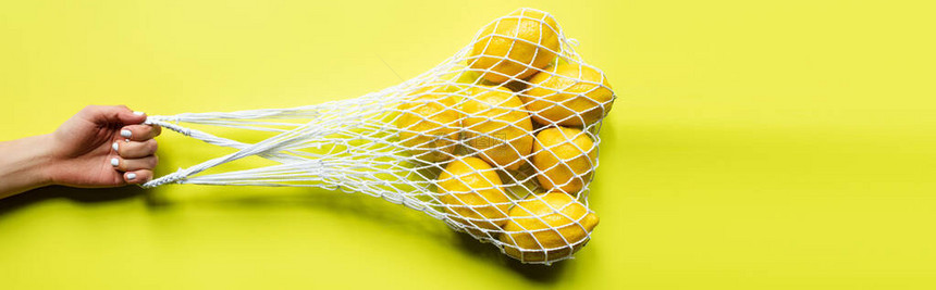 黄色背景将整片柠檬装在绳子袋里的妇图片