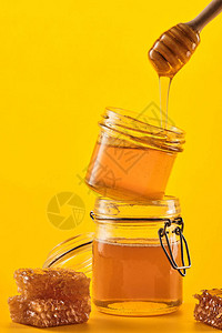 两罐蜂蜜与蜂窝和黄色背景上的一根棍子图片