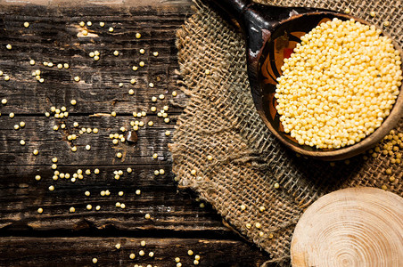 未加工的干小米散落在一个木碗上小米未煮过的谷物在木桌上的木碗里健康图片