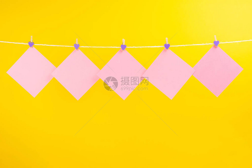 衣服线上的粉色贴纸与衣物夹隔绝在黄色背景上您图片