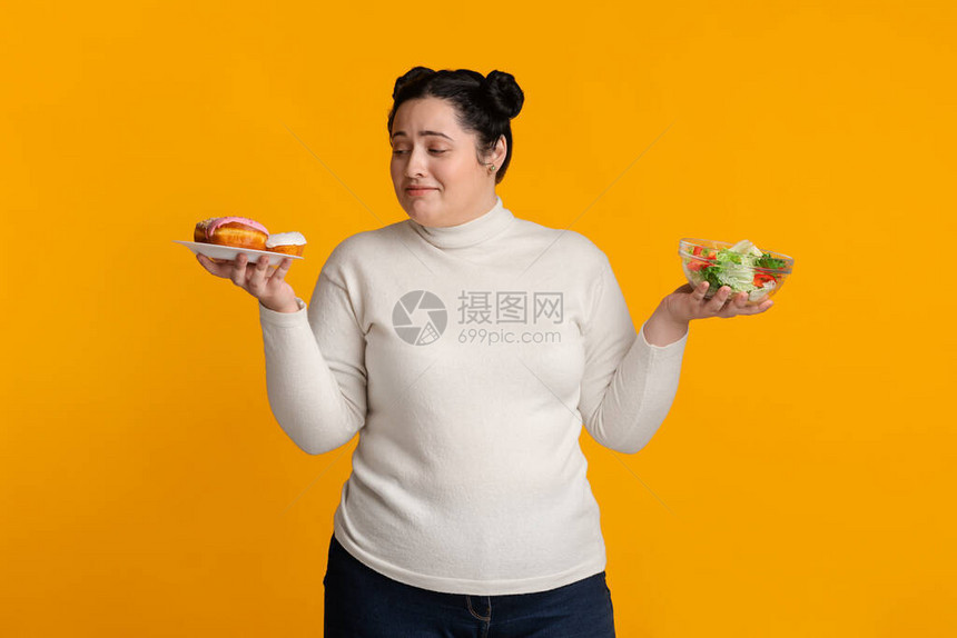 不确定的胖子女孩无法在甜圈和新鲜蔬菜沙拉之间做出抉择图片