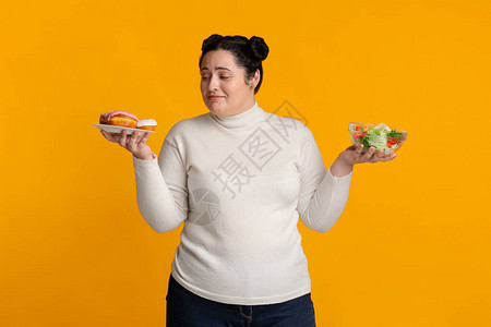 不确定的胖子女孩无法在甜圈和新鲜蔬菜沙拉之间做出抉择图片