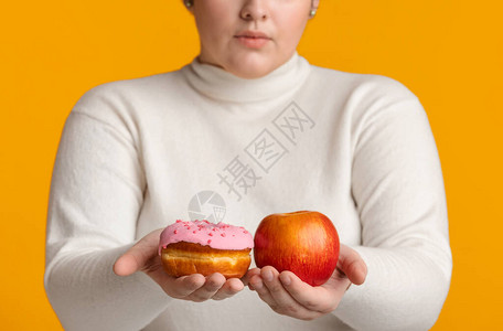 无法辨认的超重女孩手里拿着甜圈和苹果图片