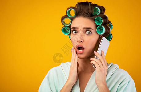 惊吓女孩与Curlers在电话上交谈在黄色工作室背景上站得很图片