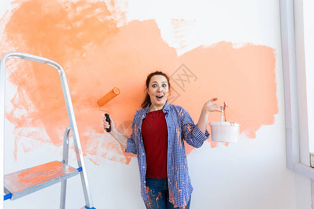 美丽笑容的年轻女子用彩色滚机在家庭内部墙壁上绘画图片