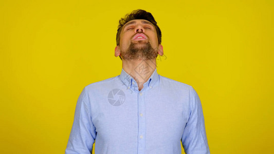 穿着蓝衬衫的胡子男闭着眼睛对黄色背景图片