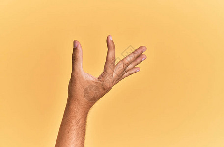 在黄色孤立的背景上抓取隐形物用手指握着物体显示太空间的手举着天花板图片