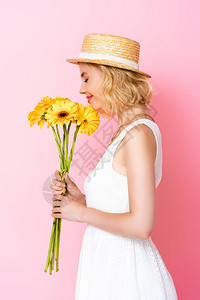 身戴草帽和白裙子的女人的侧面闻着粉红色黄图片