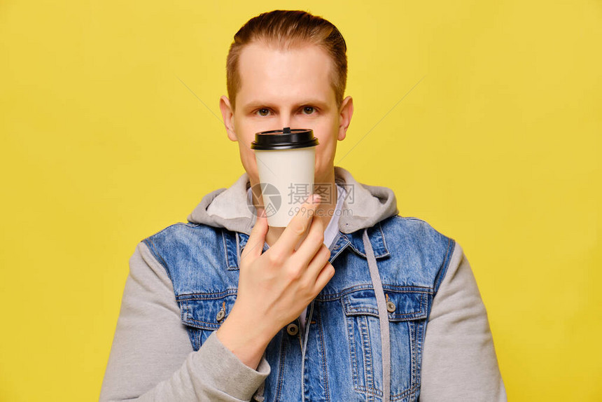 穿黄底牛仔裤的时髦白人男子复制空间近一点手持可支配纸杯咖啡遮盖半个脸部图片