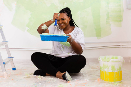 美丽的非洲裔美国女孩用油漆滚筒粉刷墙壁一个年轻漂亮的女人在她的新公寓里画墙的画像重新装背景图片