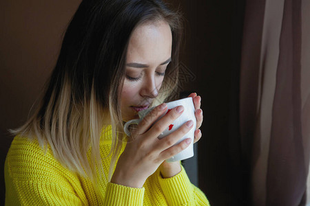 穿黄色衣服的漂亮女人手里拿着杯子在窗图片