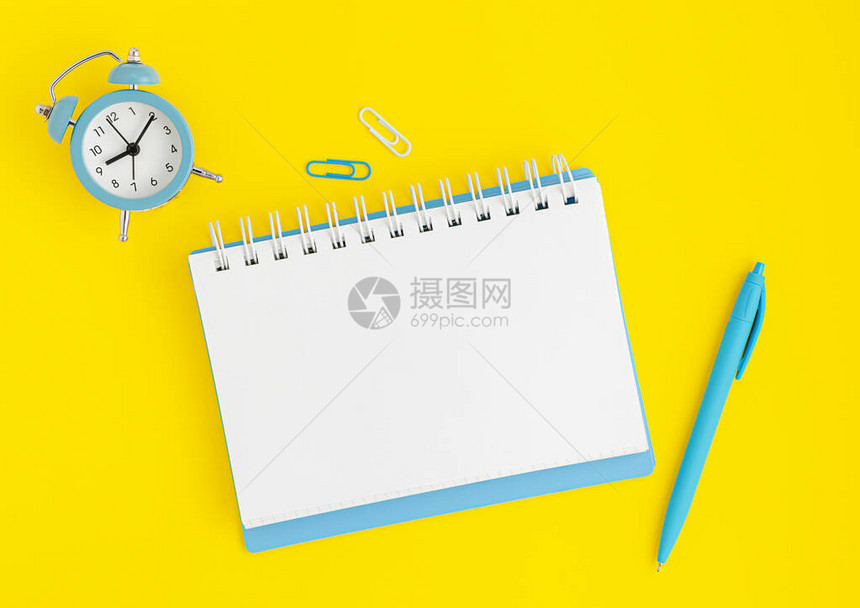 蓝色时钟笔记本空白和黄色背景上的笔图片