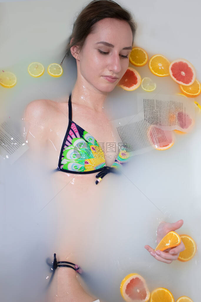 穿着鲜艳泳衣的女人在牛奶浴里放着橙子柠檬葡萄柚和书页健康水润的皮肤时装模特女孩水疗和护肤理念春天的颜色黄色图片