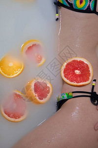 女人的身体在用橙子柠檬和葡萄柚做牛奶浴健康水润的皮肤时装模特女孩水疗和护肤理念春天的颜色黄色背景图片