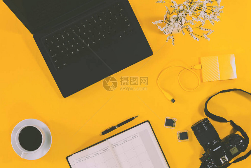 概念工作区笔记本电脑和咖啡杯带笔和相机的笔记本带有USB的外部硬盘在柔和的背景黄色上顶视图图片