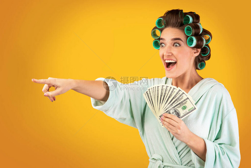 极感激动的家庭主妇持有金钱现金指针在黄室工作室背景上玩弄图片