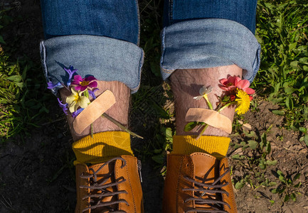 男人穿着黄色鞋子的双腿站在绿色的草地上黄色和粉红色的春天花朵用图片