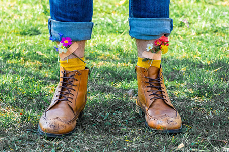 男人穿着黄色鞋子的双腿站在绿色的草地上黄色和粉红色的春天花朵用图片