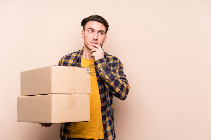 年轻caucasian男子拿着箱子放松想着一些东西看图片