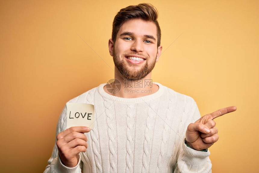 年轻金发的浪漫男子长着胡子和蓝眼睛拿着纸与爱情信息用手和指向另图片
