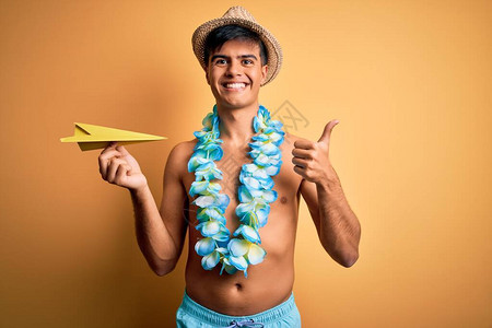 度假时穿着泳装和夏威夷花环的年轻游客拿着纸飞机开心地笑着做ok手势图片