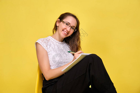 女孩在黄色背景上戴着眼镜笑着的老师坐在笔记本图片
