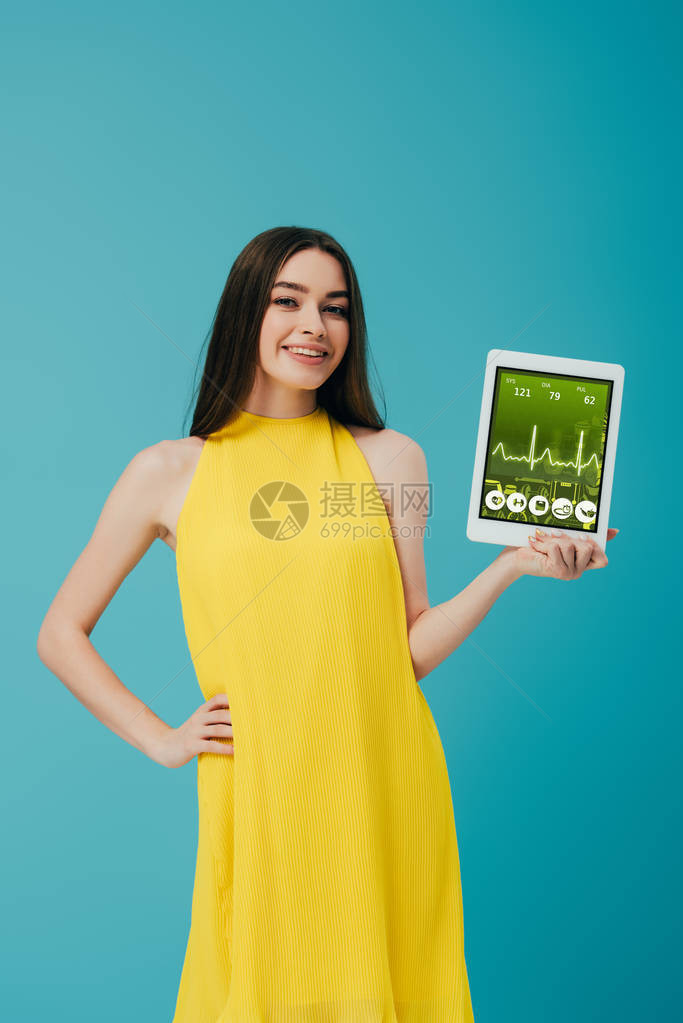 身着黄裙子的棕褐色笑脸女孩展示数字平板电脑和在绿石上隔离的图片