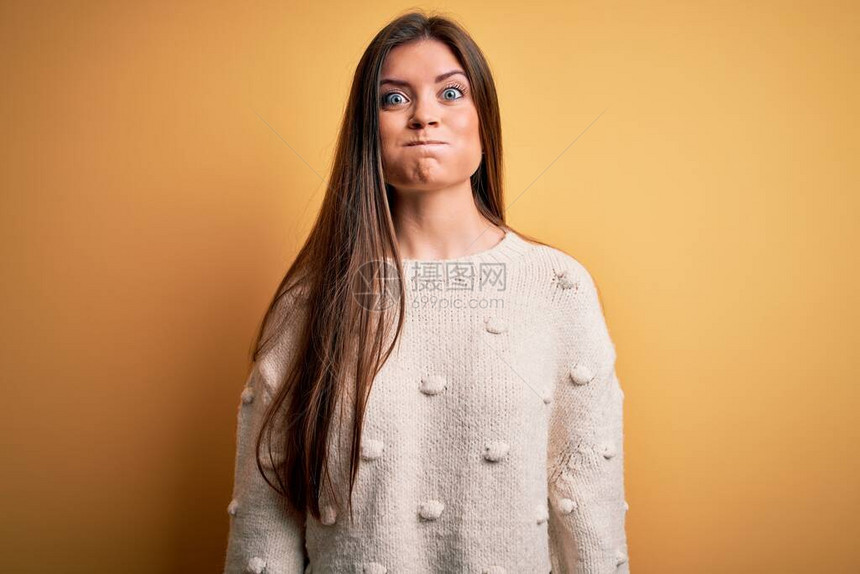 蓝眼睛的年轻美女穿着随身毛衣站在黄色背景上图片