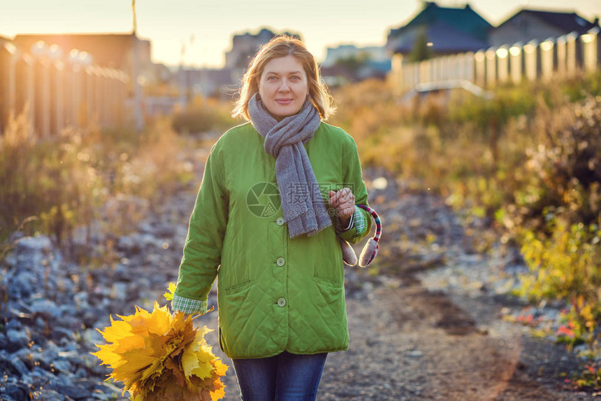 一个拥有秋叶花束的快乐女人在一个秋天走在村里街道上图片