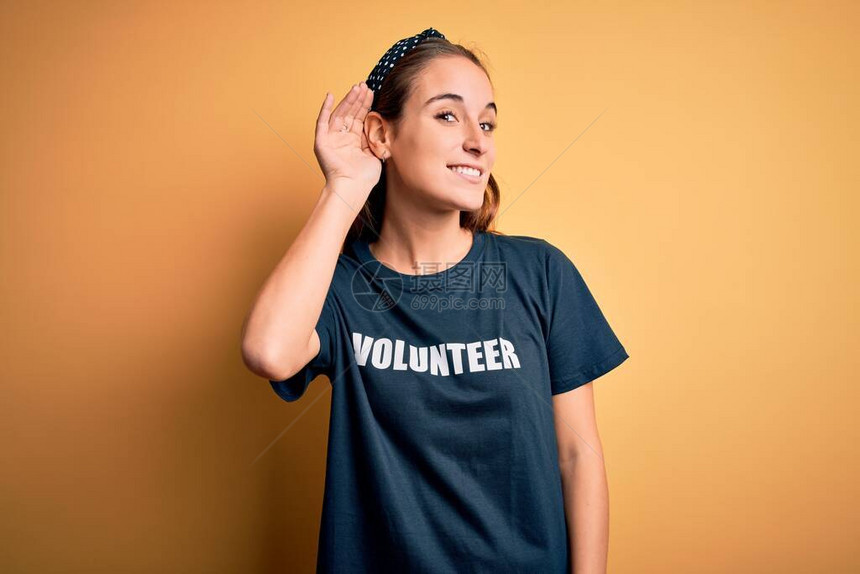 年轻漂亮的女人穿着志愿者T恤在黄色背景下做志愿者图片