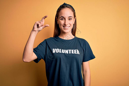 年轻漂亮的女人穿着志愿者T恤在黄色背景上做志愿者图片