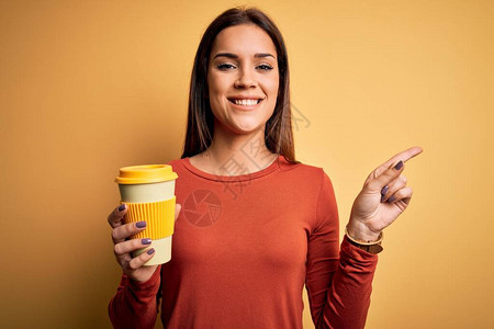 在黄色背景下喝杯外卖咖啡的褐发美女图片