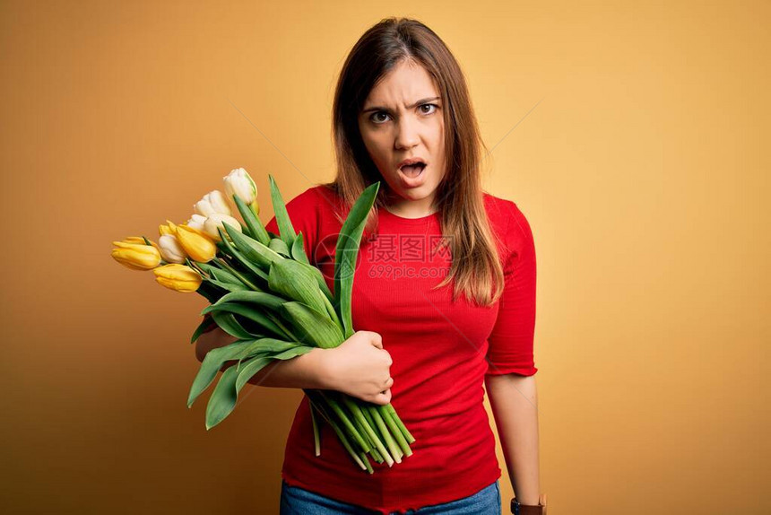 年轻的金发女子在黄色背景上拿着浪漫的郁金香花束图片
