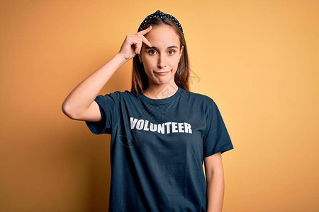 身穿志愿人员T恤衫的年轻美女在黄色背景下从事志愿工作图片