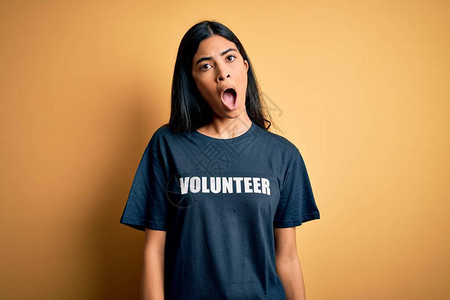 年轻漂亮的西班牙裔女穿着志愿者T恤作为社会慈善道德在震惊的脸上图片