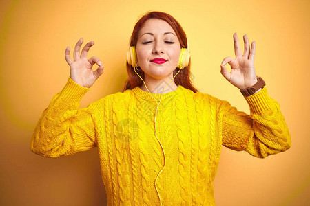 年轻的红发女人用耳机在黄色的孤立背景上听音乐图片