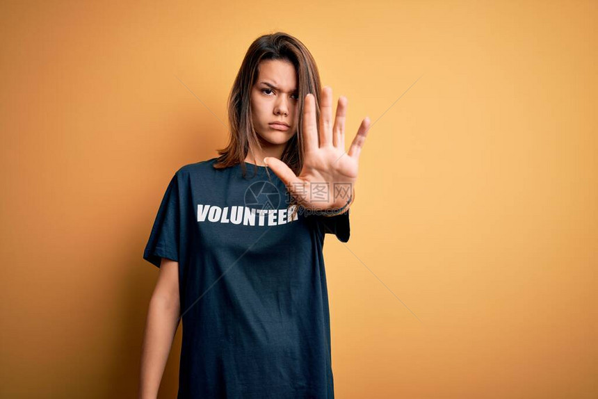 年轻漂亮的黑发女孩做志愿者穿着t恤与志愿者留言词做停止用手掌脸上带着消极和严肃的图片