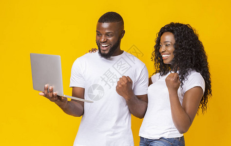 带着笔记本电脑在黄色背景上微笑空地上笑着庆祝成功的非洲千年男图片