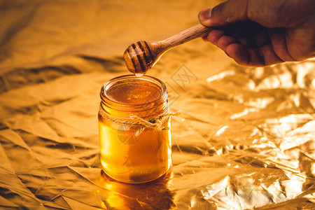 蜂蜜在玻璃瓶和金本底图片