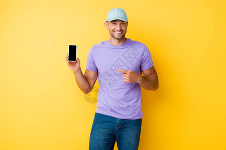 穿着蓝帽子的快乐男人用手指着智能手机黄背景图片