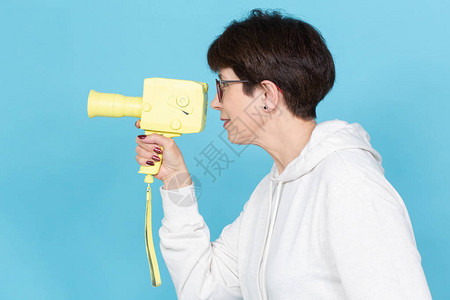 身份不明的女人拿着黄色老式电影摄机摆在蓝色背景上艺术和爱好的概图片